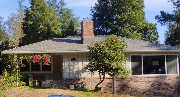 Exterior view of a single-family house with a chimney and a new asphalt shingle roof installation