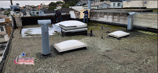 Workers repairing a flat roof with skylights and ventilation pipes, with the One Way Roofing logo visible.