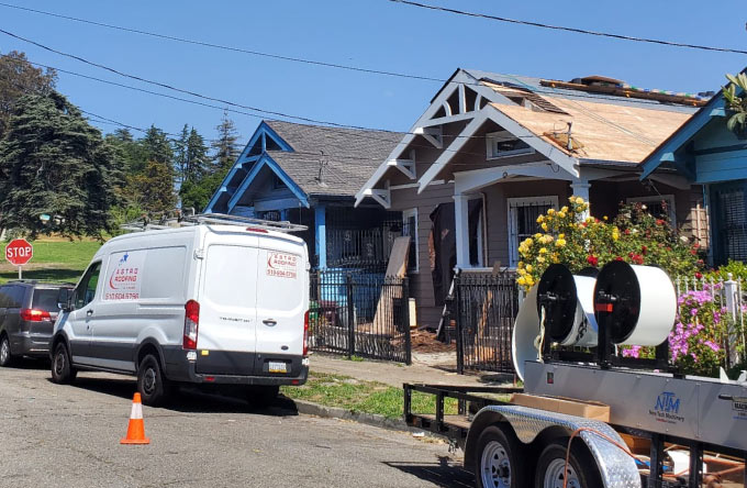 Astro Roofing work truck parked in front of homes in Oakland, with a house showing a partially stripped roof ready for replacement