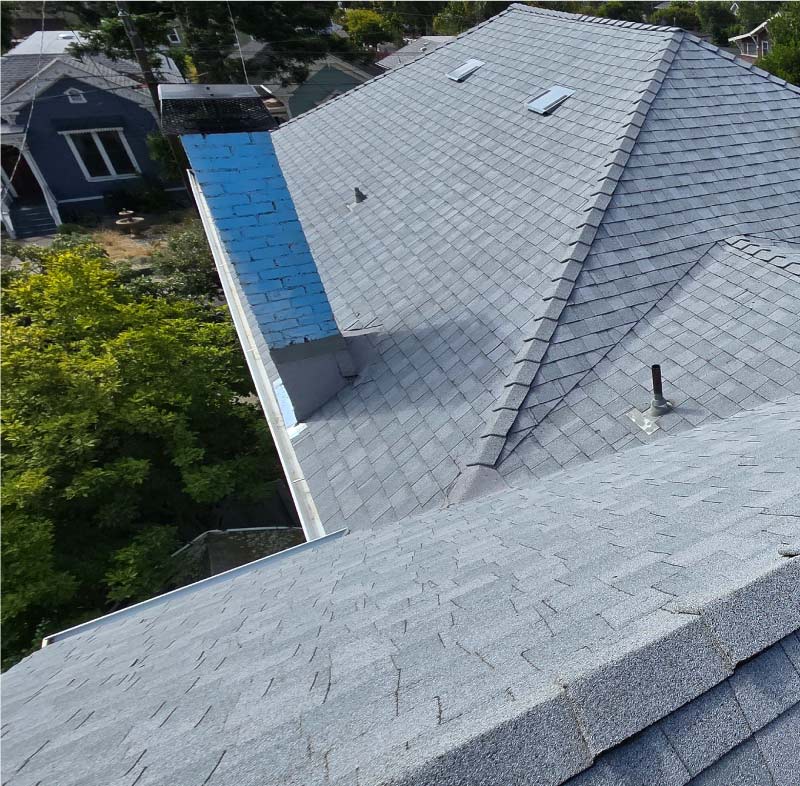 igh-angle view of a new asphalt shingle roof with custom chimney flashing and seamless gutter installation service on a Bay Area property.