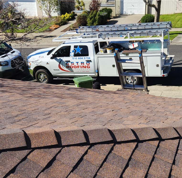 Branded Astro Roofing service truck with ladder rack parked curbside during a residential roof installation project.