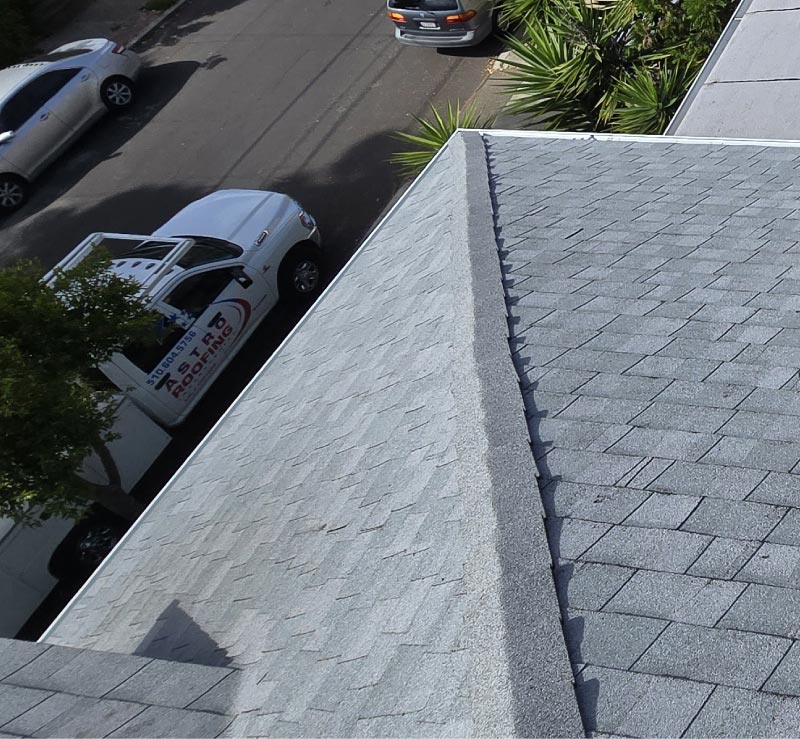 alt="Astro Roofing service van parked beside a newly installed gray asphalt shingle roof in Oakland, CA"